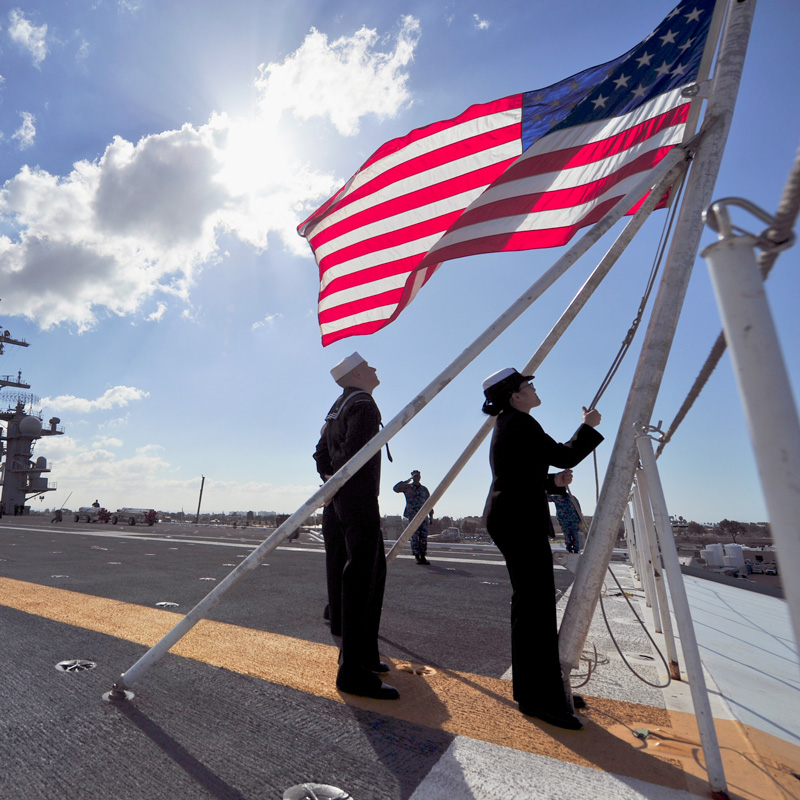 To uniformed persons raise an American flag over their ship.